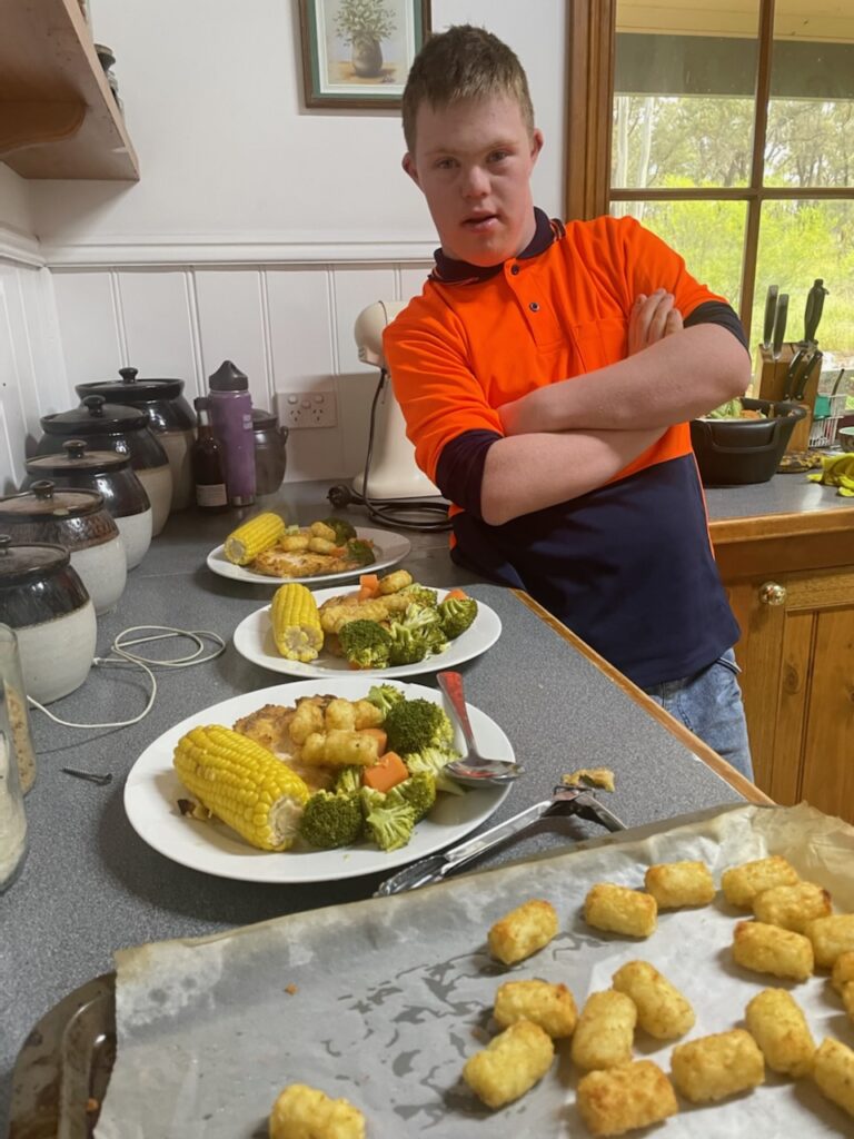 Daniel stands proudly in the kitchen behind the plate of vegetables and chicken he has prepared for his family. 